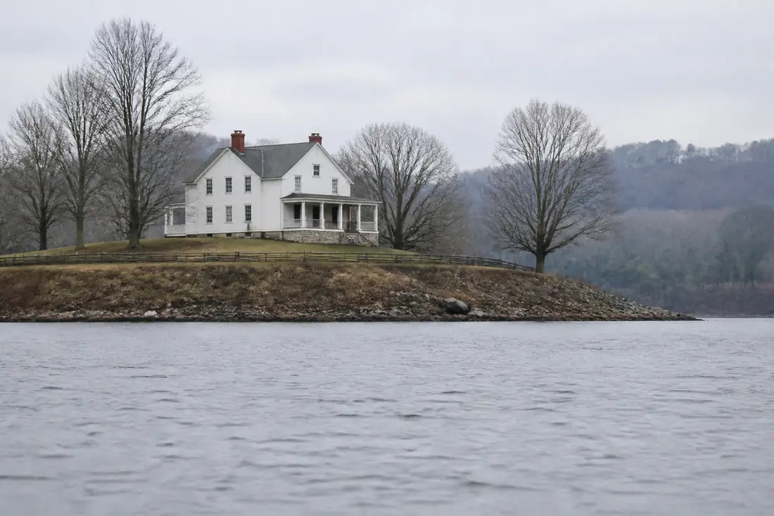 A white clapboard farmhouse on a low bluff seen from across open water