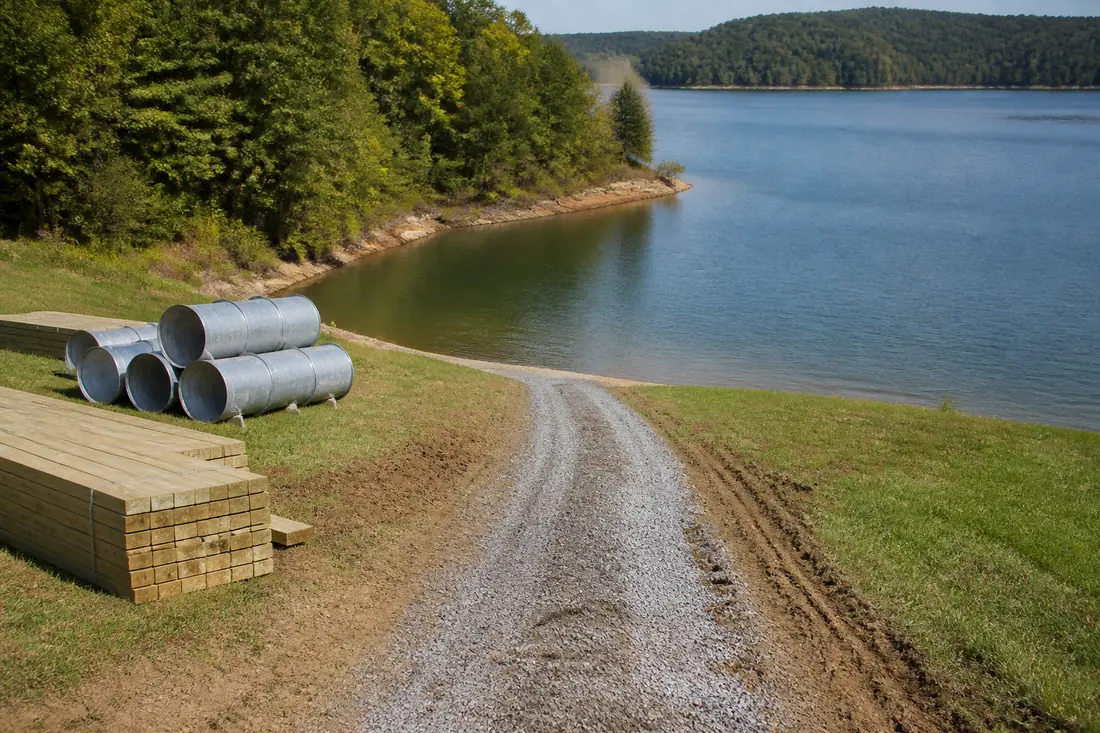 A gravel access track and stacked dock materials on the grass above a lake shoreline
