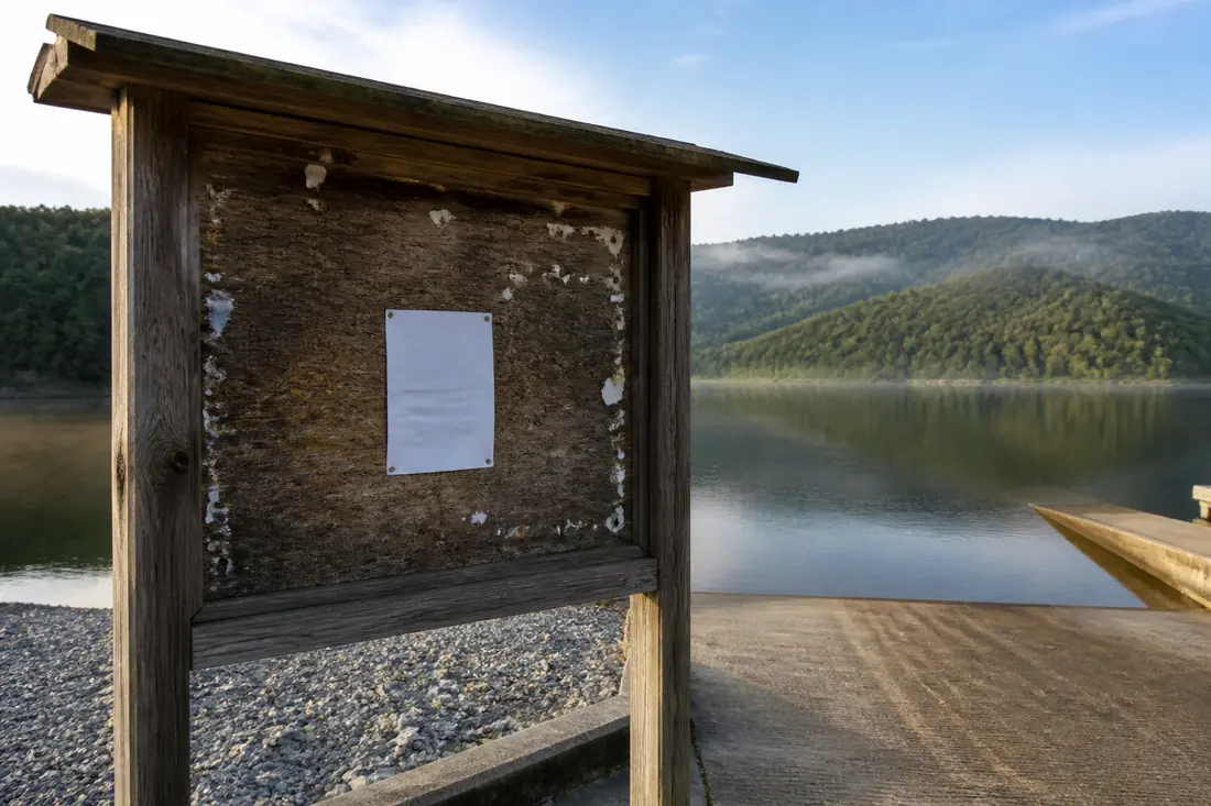 A public notice posted on a board beside a lake shoreline